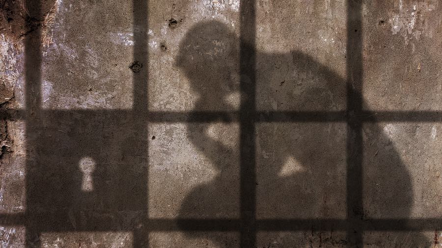 a shadow of a man sitting in a jail cell