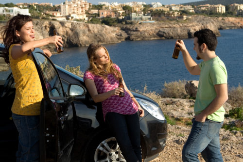 three people standing near a car with a bottle of beer