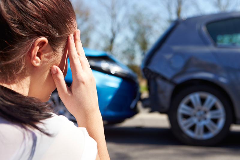 a woman is holding her head in front of a car that has been damaged