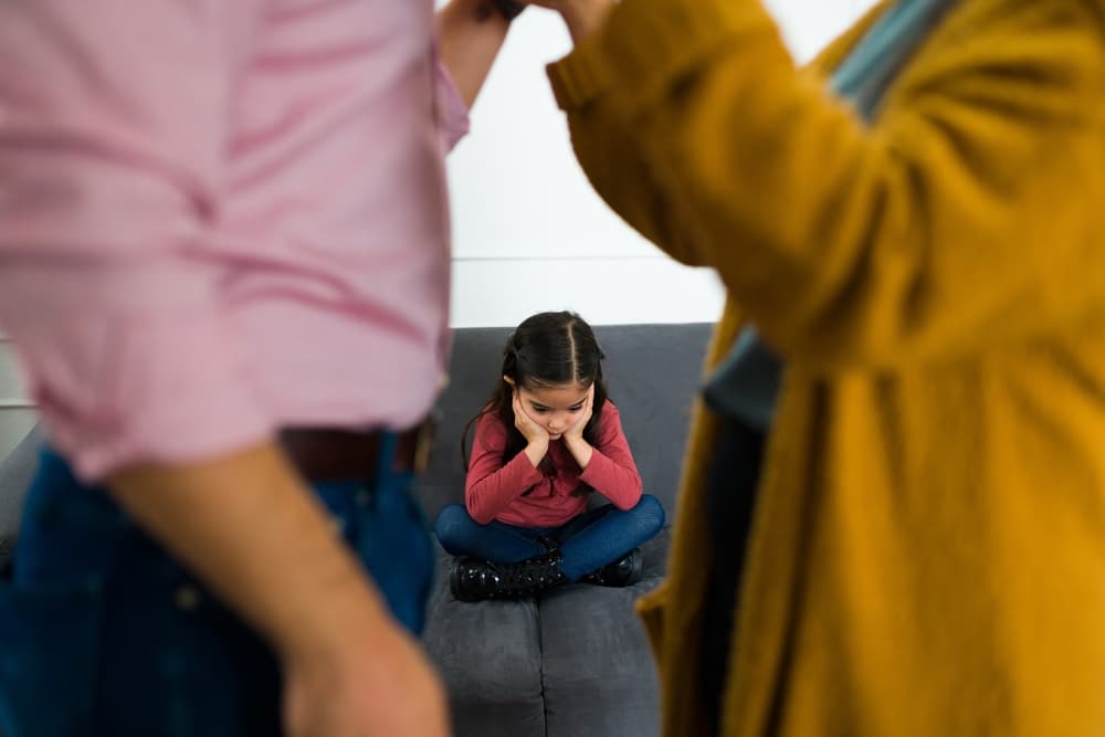 Upset child caught in the midst of her parents' dispute over child custody following a divorce, experiencing the emotional strain of the situation.