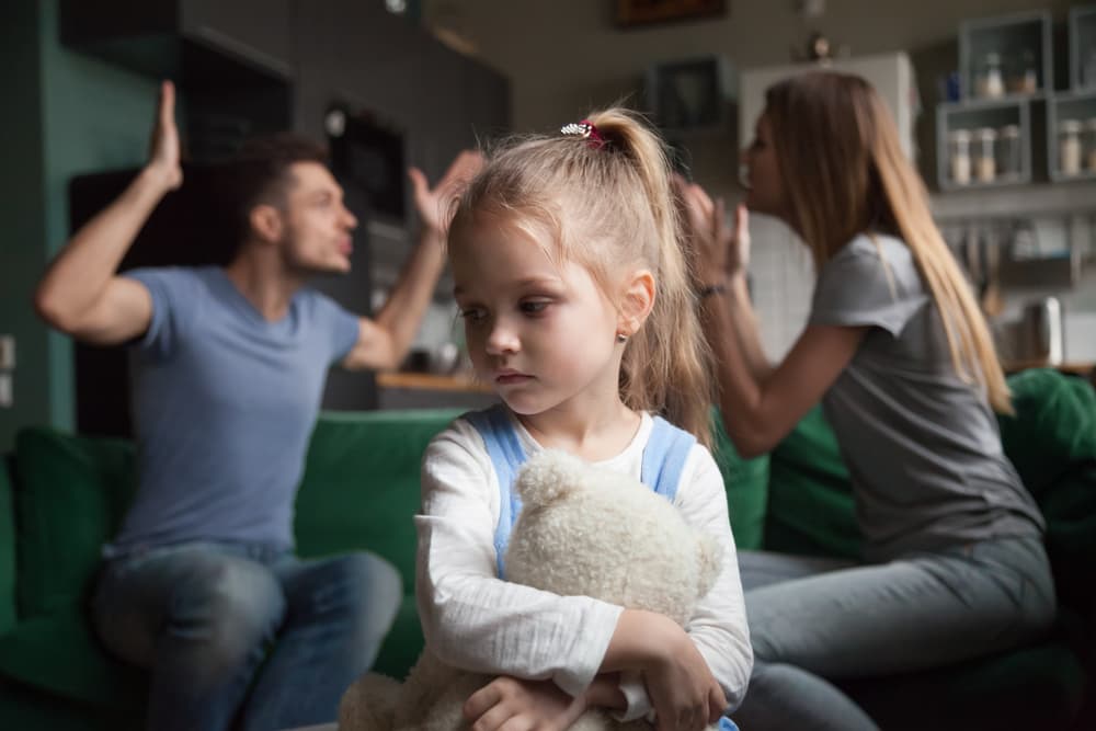 Unhappy child witnessing parental conflict, upset girl affected by mom and dad arguing. Illustrates family conflicts, divorce impact on children concept.