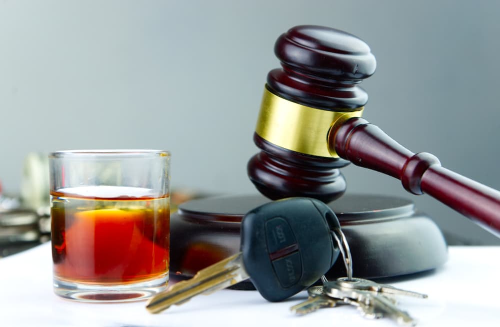 A judge's gavel beside a whiskey glass and car key, representing the concept of driving under the influence (DUI).