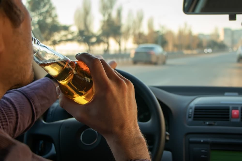 A man drinking alcohol behind the wheel, illustrating the dangers of drunk driving.