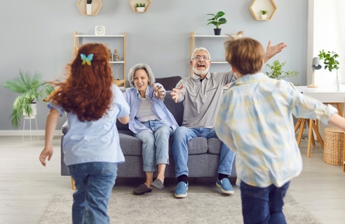 Happy grandparents sitting on a couch with open arms as their grandchildren run toward them, symbolizing family bonding and connection.