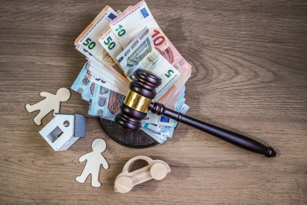 Judge's gavel on Euro banknotes with wooden figures of house, car and people.