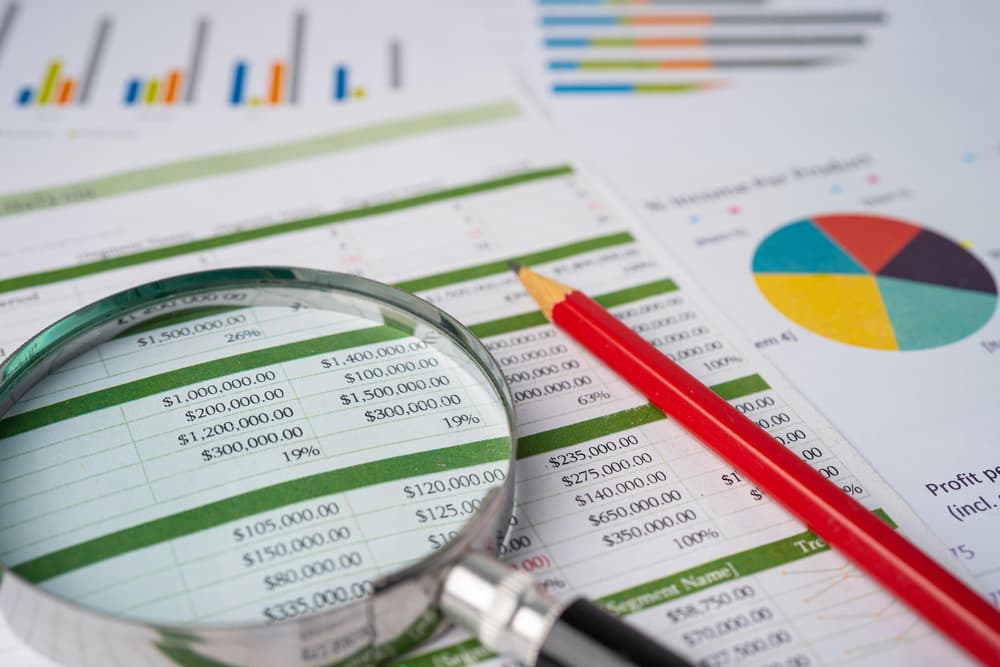 Magnifying glass with pencil on spreadsheet table and graph paper;