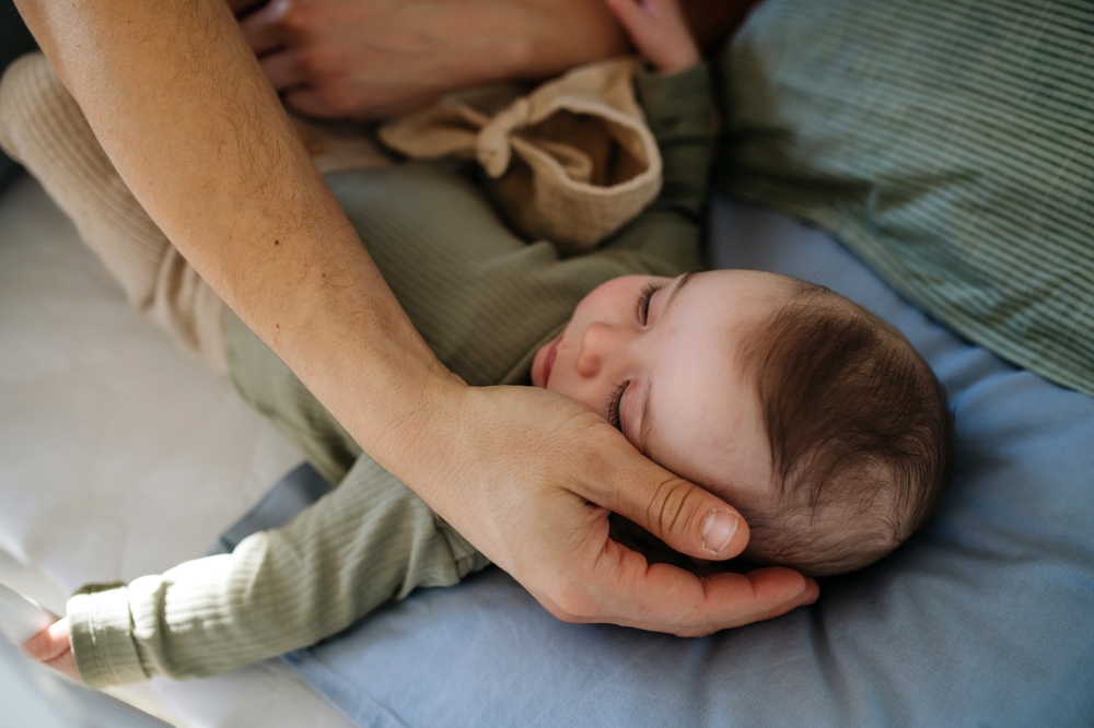 Close-up of father's hands putting baby in bed